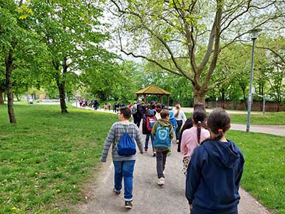 Eine große Gruppe von Kindern läuft vor der Fotografin durch einen grünen Park.